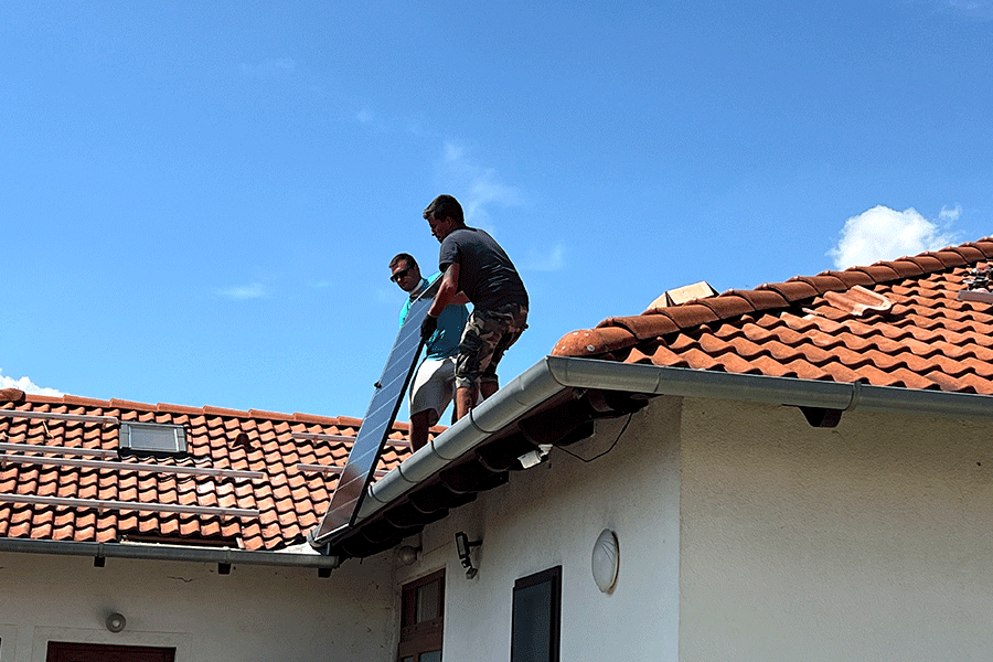 Εργάτες μεταφέρουν ένα μονοκρυσταλλικό φωτοβολταϊκό πάνελ IBC στην οικιακή στέγη για εγκατάσταση.